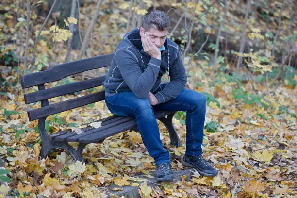 depressed man sits on bench in the autumn forest