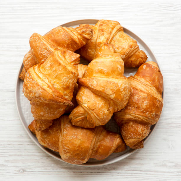istock Fresh croissants on grey round plate on white wooden table, overhead view. From above, flat lay, top view. 1066876856