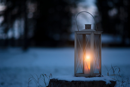 Candle lantern in snow against defocused forest background.