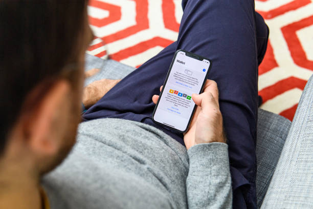 Man using latest iPhone XS unboxing display wallet London: Man using on his living room sofa the new Apple iPhone Xs with the immense OLED retina display and a12 bionic chip, looking over the app application wallet on his living room sofa mac plus stock pictures, royalty-free photos & images