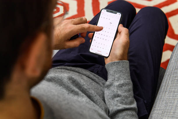 Man using latest iPhone XS unboxing display calendar app London: Man using on his living room sofa the new Apple iPhone Xs with the immense OLED retina display and a12 bionic chip, looking over the app application calendar app mac plus stock pictures, royalty-free photos & images