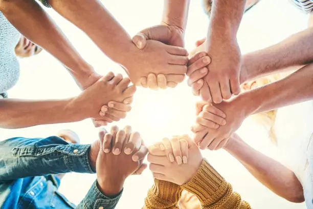 Closeup shot of a diverse group of people holding hands together in unity
