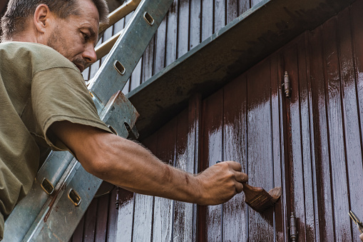 Adult Man Painting an Old House With Protective Paint.