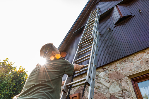 Adult Man Setting a Ladder for Cottage Renovation.