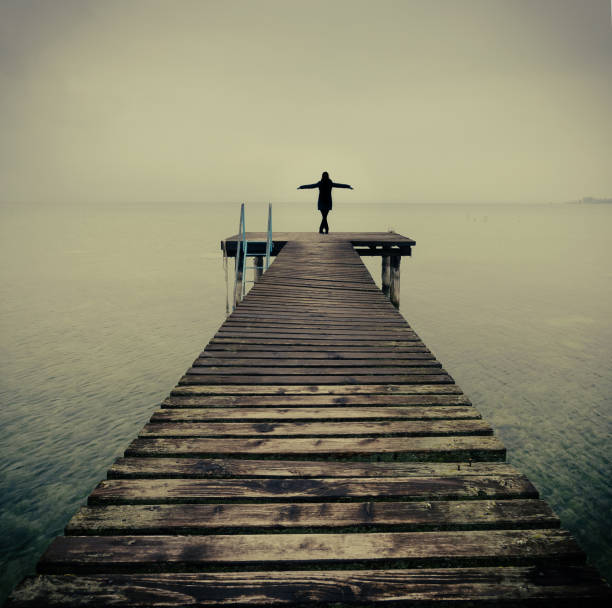 Silhouette of one young woman alone with arms outstretched at end of wooden pier peaceful Lake Garda, Italy - fine art style