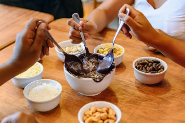 Three hands dipping into bowl of sauce with small bowls of nuts and seeds, traditional Brazilian food