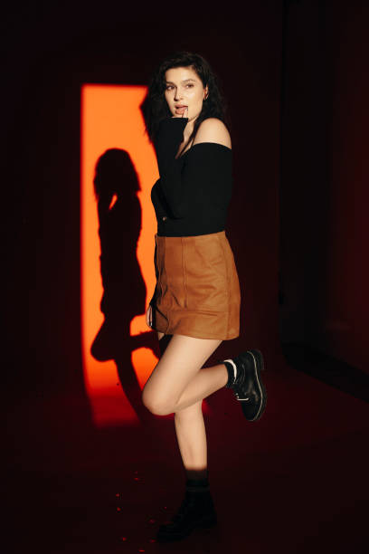 istock Side view of charming young female touching lips and looking away while standing in dark room. Flirty woman looking away 1066923020