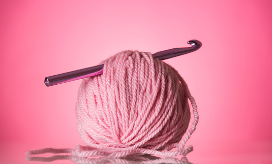 Bright pink ball of wool and a crochet hook on a pink background