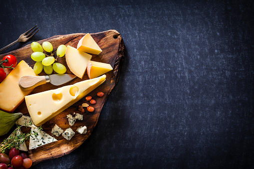 Cheese board shot from above on rustic table. The composition is at the left of an horizontal frame leaving useful copy space for text and/or logo at the center-right. Predominant color is brown. Low key DSRL studio photo taken with Canon EOS 5D Mk II and Canon EF 100mm f/2.8L Macro IS USM.