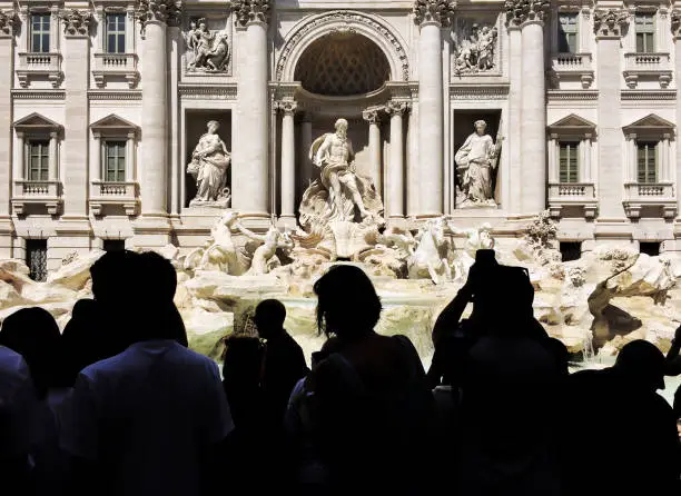 Silhouettes of tourists looking at the famous Trevi Fountain in a sunny day in Rome