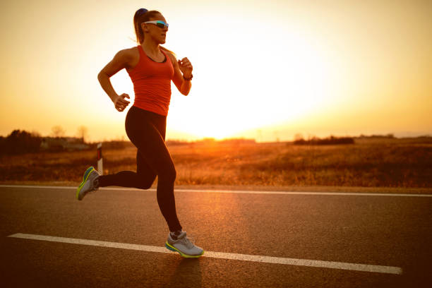 sportler-frau läuft auf der straße bei sonnenuntergang - road running stock-fotos und bilder