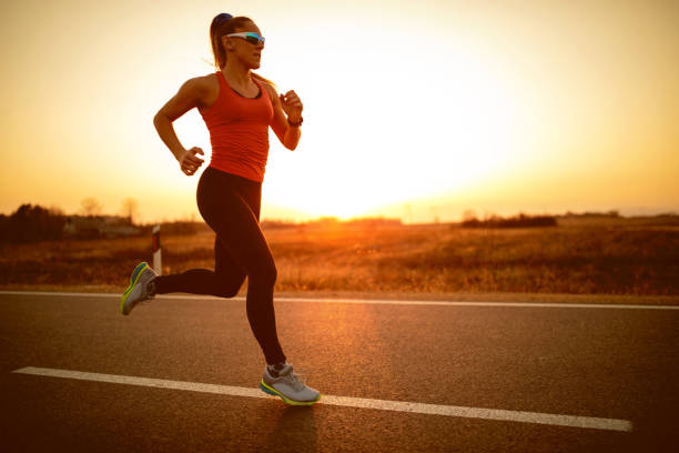 спортсменка, бегущая по дороге на закате - road running стоковые фото и изображения