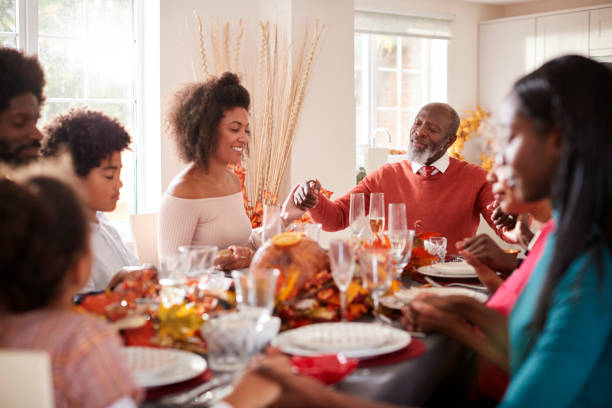 famiglia di razza mista multigenerazionale che si tiene per mano e dice grazia prima di mangiare al loro tavolo da pranzo del ringraziamento, messa a fuoco selettiva - saying grace immagine foto e immagini stock