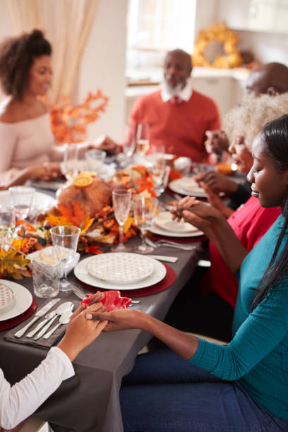 istock Multi generation mixed race family holding hands and saying grace before eating at their Thanksgiving dinner table, selective focus, vertical 1066944110