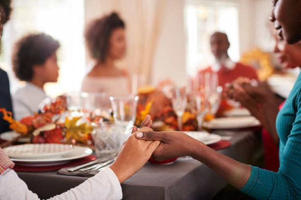 jovem adulta preta e a filha dela, de mãos dadas e dizendo graça com sua família de geração multi na mesa de jantar de ação de graças, detalhe, foco em primeiro plano - family thanksgiving dinner praying - fotografias e filmes do acervo