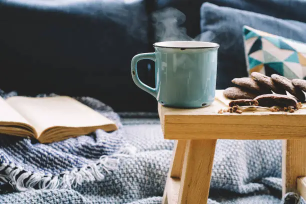 Photo of Cup of hot drink on wooden table. Living room interior with blue sofa on background.