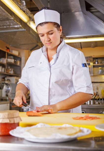 istock Young female chef coock dressed in white uniform cut salmon fish on the table in restaurant kitchen 1066953888
