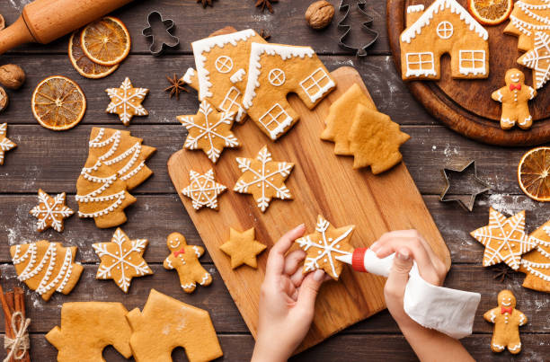 Icing process of Christmas bakery. Unrecognizable woman decorating homemade cookies Icing process of Christmas bakery. Unrecognizable woman decorating homemade gingerbread cookies on wooden table, top view christmas cookies stock pictures, royalty-free photos & images