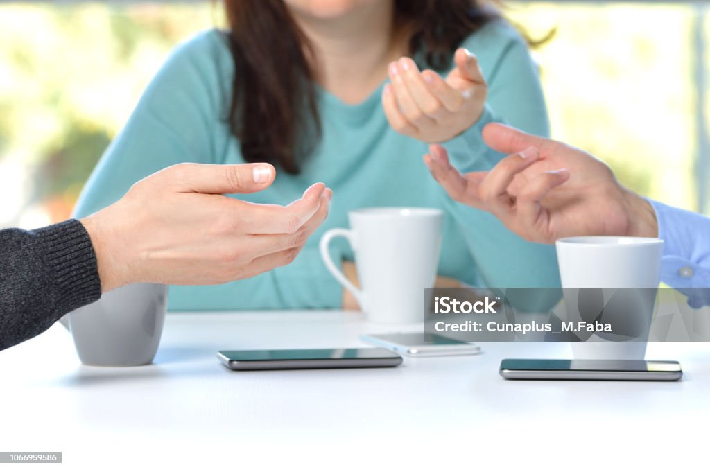 coffee in good company Three friends hands talking in a bar and disconnected from social networks with the phone on the table Adult Stock Photo