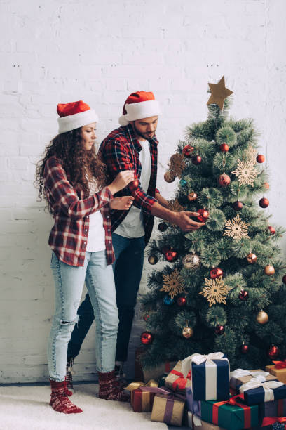istock couple in santa hats decorating christmas tree at home 1066961448