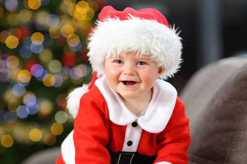 Baby wearing santa claus disguise looking at camera in christmas on a couch in the living room at home