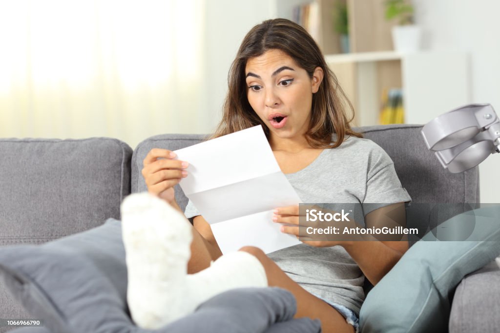 Surprised disabled girl reading notification Surprised disabled girl reading notification  sitting on a couch in the living room at home Financial Bill Stock Photo
