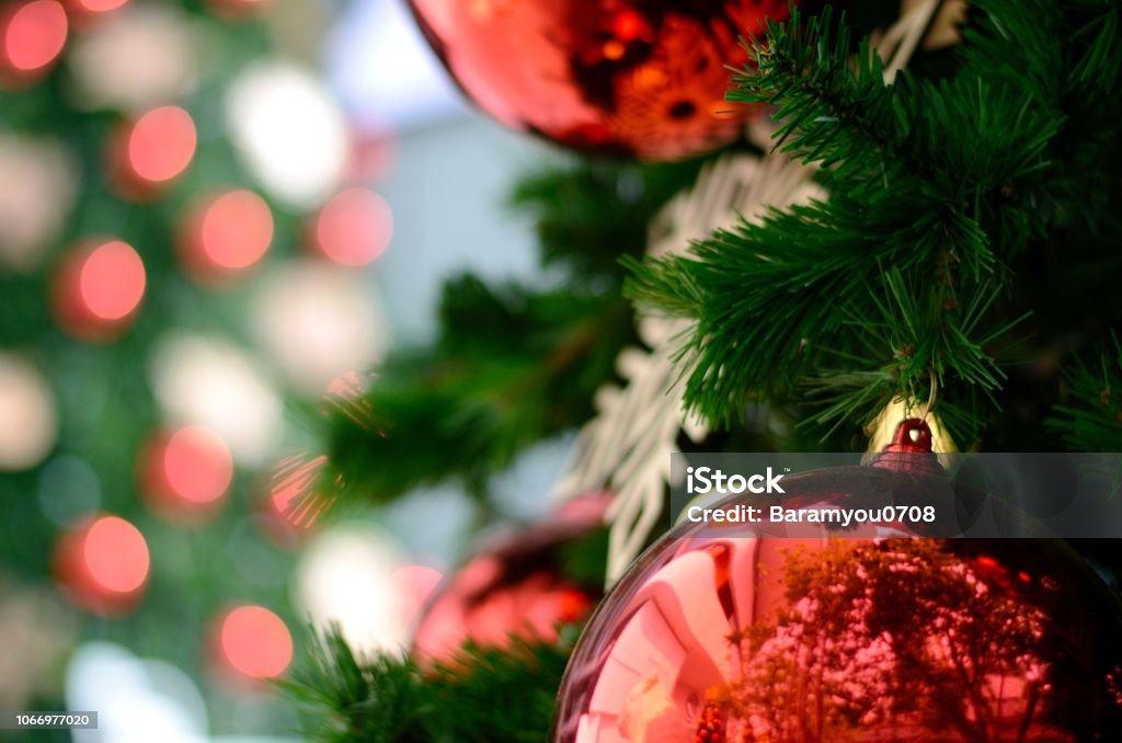Red bauble and other ornament hanging on Christmas tree with bokeh background from another Christmas tree with space for text. Christmas Tree Stock Photo