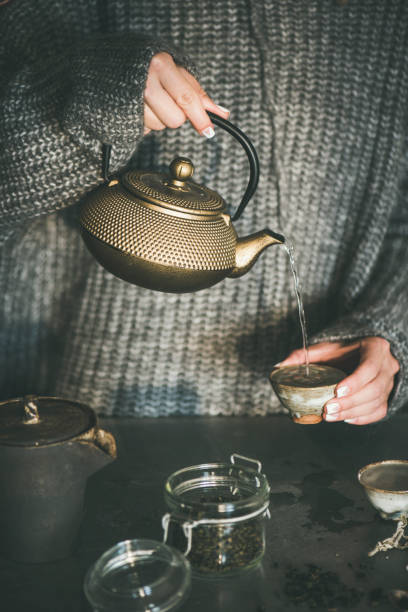 istock Female in sweater pouring green tea from pot into cup 1066977806