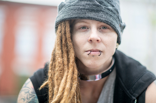 A woman with punk style is looking into the distance. She has dreadlocks, a toque and piercings.