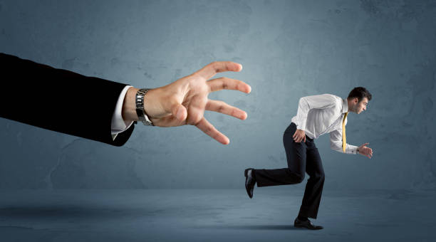istock Business man running away from a huge hand concept 1066981530