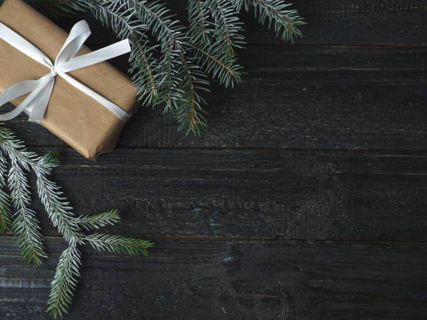 istock Christmas gift with white ribbon on black background with Christmas tree branches 1066981950