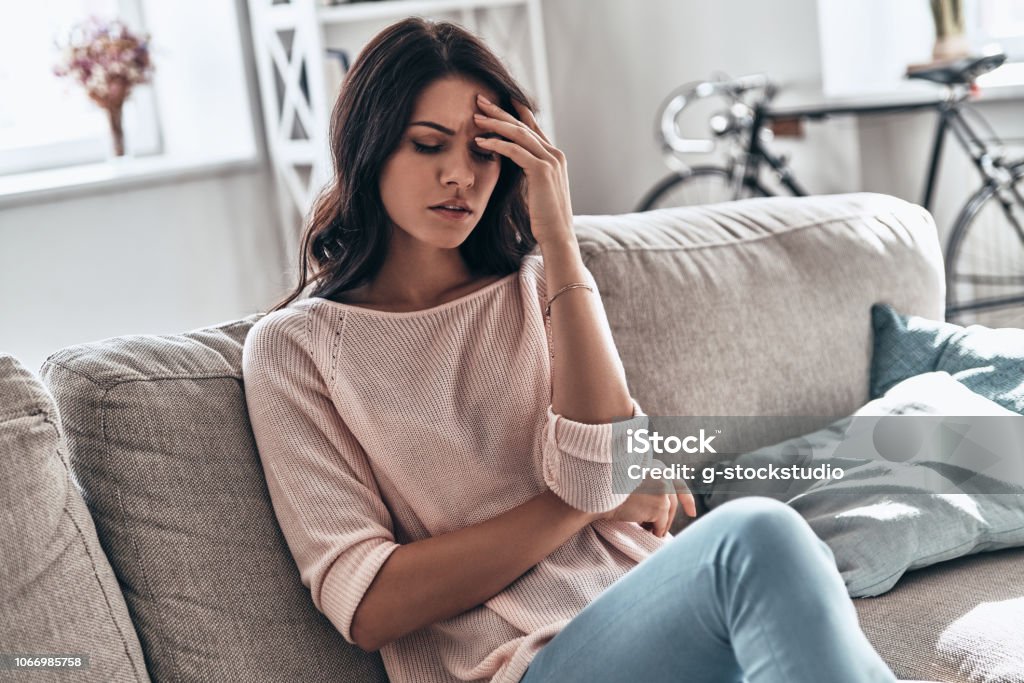 Feeling bad. Frustrated young woman suffering from the headache while sitting on the sofa at home Women Stock Photo