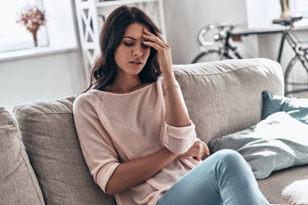 Feeling bad. Frustrated young woman suffering from the headache while sitting on the sofa at home digestive system photos stock pictures, royalty-free photos & images