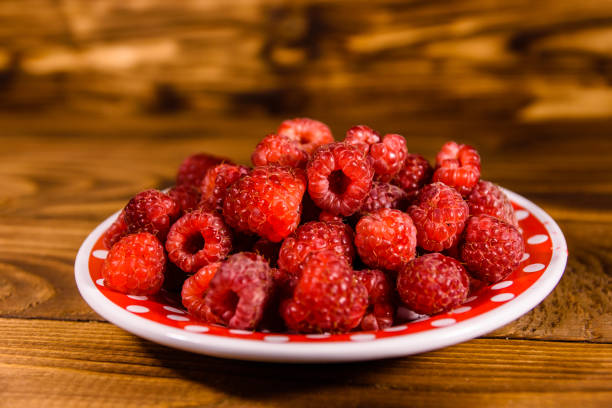 istock Ceramic plate with ripe raspberries on wooden table 1066985974
