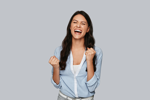 Attractive young woman punching the air and smiling while standing against grey background