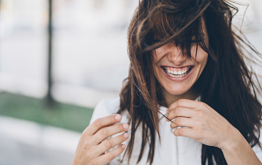Beautiful charming woman with messy hair laughing outdoor in windy day