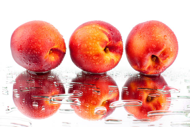 tre pesche su una superficie a specchio bianca in gocce d'acqua isolate macro - peach nectarine wet drop foto e immagini stock
