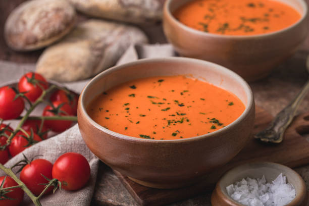 Tomato soup and homebaked bread Tomato soup still life with rustic ciabatta bread and fresh tomatoes. The bowl in focus is on a small wooden cutting board. There is a linen cloth next to the bowl, and a small bowl of sea salt. tomato soup stock pictures, royalty-free photos & images