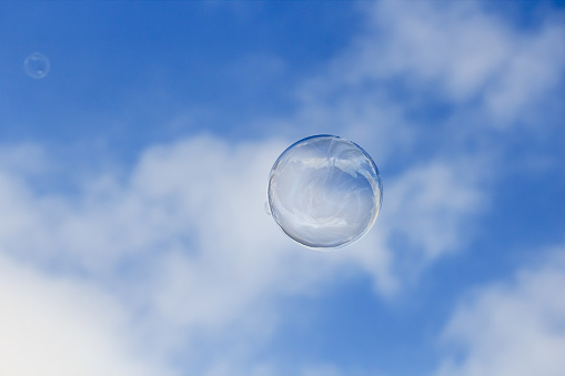 A soap bubble is floating in the air isolated on cloudy blue sky