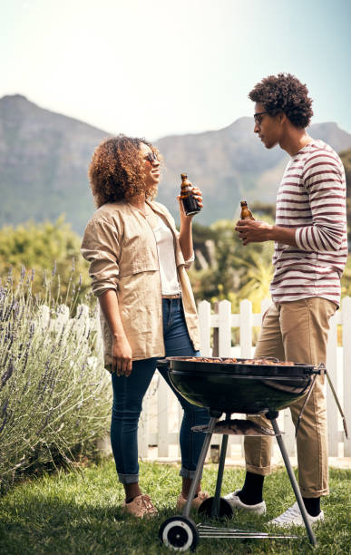 This is what summer's about Shot of a young couple drinking beer while having a barbecue together south african braai stock pictures, royalty-free photos & images