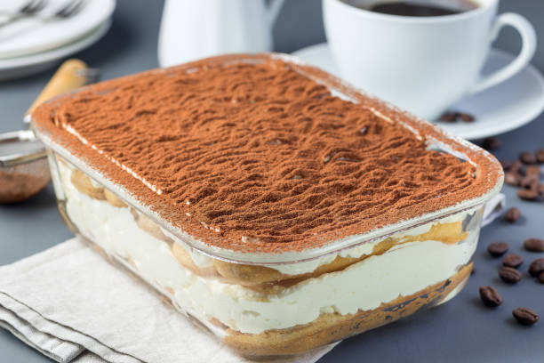 Traditional italian Tiramisu dessert cake in a glass form, decorated with cocoa powder with coffee cup, on gray background, horizontal stock photo