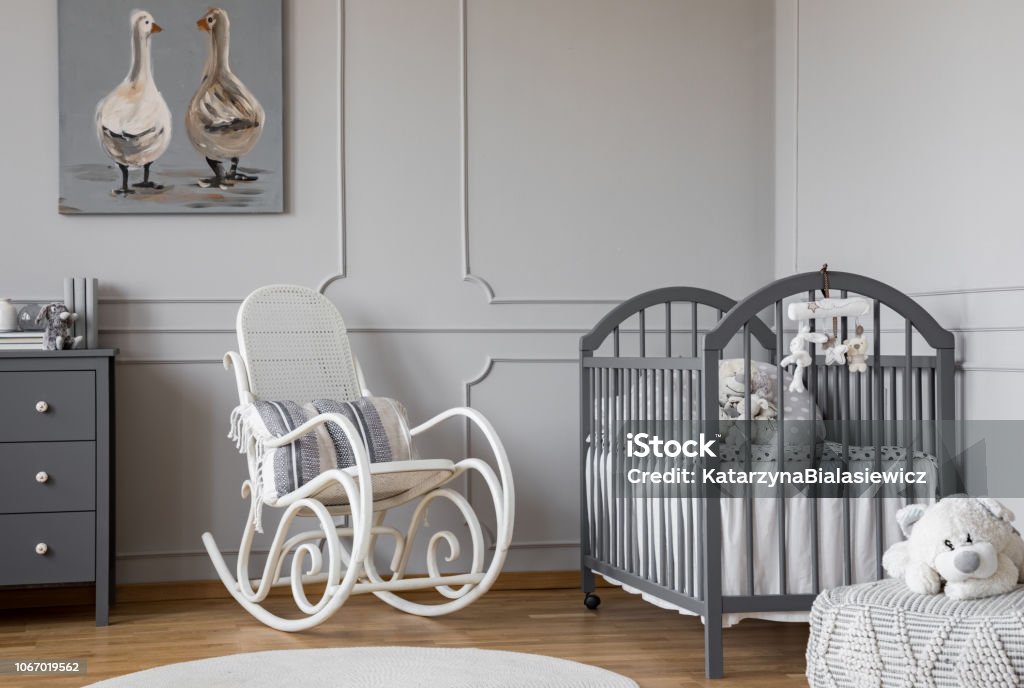 Weißer Schaukelstuhl mit Kissen neben Holz Wiege in eleganten Babyzimmer mit Ente Poster an der Wand - Lizenzfrei Babyzimmer Stock-Foto