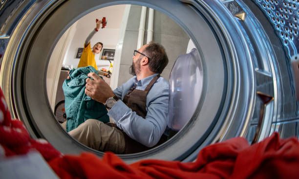 Can you help me A man is doing laundry while his son is playing with toys father housework stock pictures, royalty-free photos & images