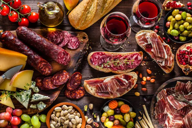 Top view of a rustic wooden table filled with delicious cheese and cold meat selection. Some fruits like figs, pears and grapes, olives, pistachios, bread, breadsticks an olive oil bottle and two wineglasses complete the composition. DSRL studio photo taken with Canon EOS 5D Mk II and Canon EF 100mm f/2.8L Macro IS USM