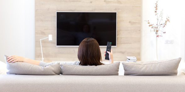 Young woman watching TV in the living room sitting on couch