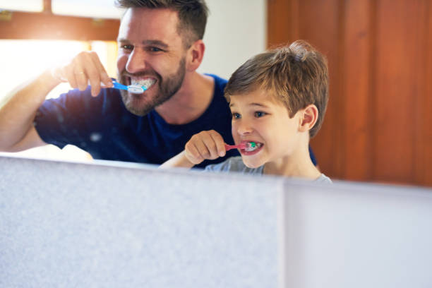 Up, down, round and round Shot of a father and his little son brushing their teeth together at home teeth bonding stock pictures, royalty-free photos & images