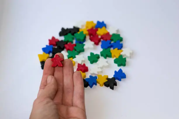 Photo of Red meeple - small figure of man in hand on white background with colorful meeples. Board game concept.