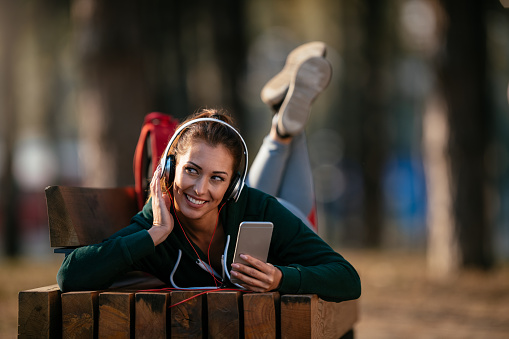Young sports woman listening music in nature. Shallow DOF. Developed from RAW; retouched with special care and attention; Small amount of grain added for best final impression. 16 bit Adobe RGB color profile.