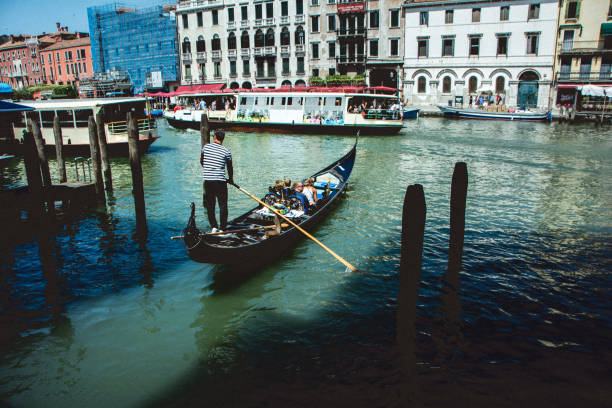 Gondola in Venice Venice, Italy - July 9, 2018 : Boats and black gondolas moving through the water canal with the tourists inside. Venice, a city in northeastern Italy and the capital of the Veneto region, is one of the most famous travel destination in the world. Gondola is a traditional, flat-bottomed Venetian rowing boat, well suited to the conditions of the Venetian lagoon.Their primary role today is to carry tourists on rides. venice italy grand canal honeymoon gondola stock pictures, royalty-free photos & images
