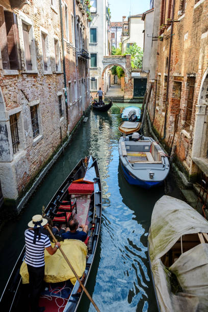 Gondola ride in Venice, Italy Venice, Italy - July 9, 2018 : Several black gondolas moving through the water canal with the tourists inside. Venice is a one of the most famous travel destination in the world, a city in northeastern Italy and the capital of the Veneto region. Gondola is a traditional, flat-bottomed Venetian rowing boat, well suited to the conditions of the Venetian lagoon.Their primary role today is to carry tourists on rides. venice italy grand canal honeymoon gondola stock pictures, royalty-free photos & images